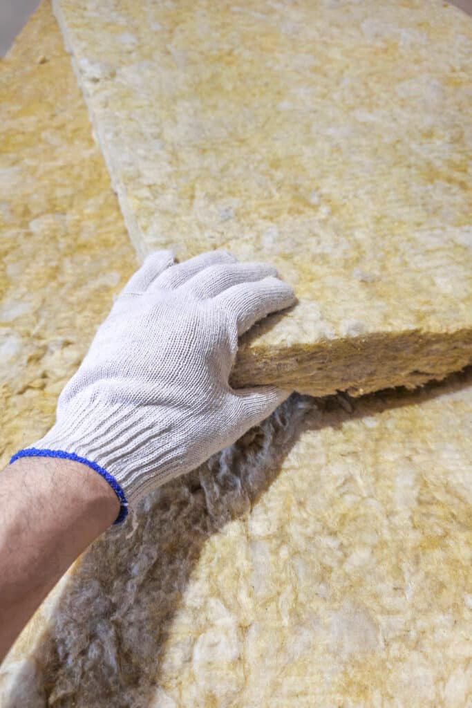 Isolation laine minérale : Installation matériaux thermique Main gantée tenant un panneau d'isolation thermique en laine minérale jaune, prêt pour l'installation