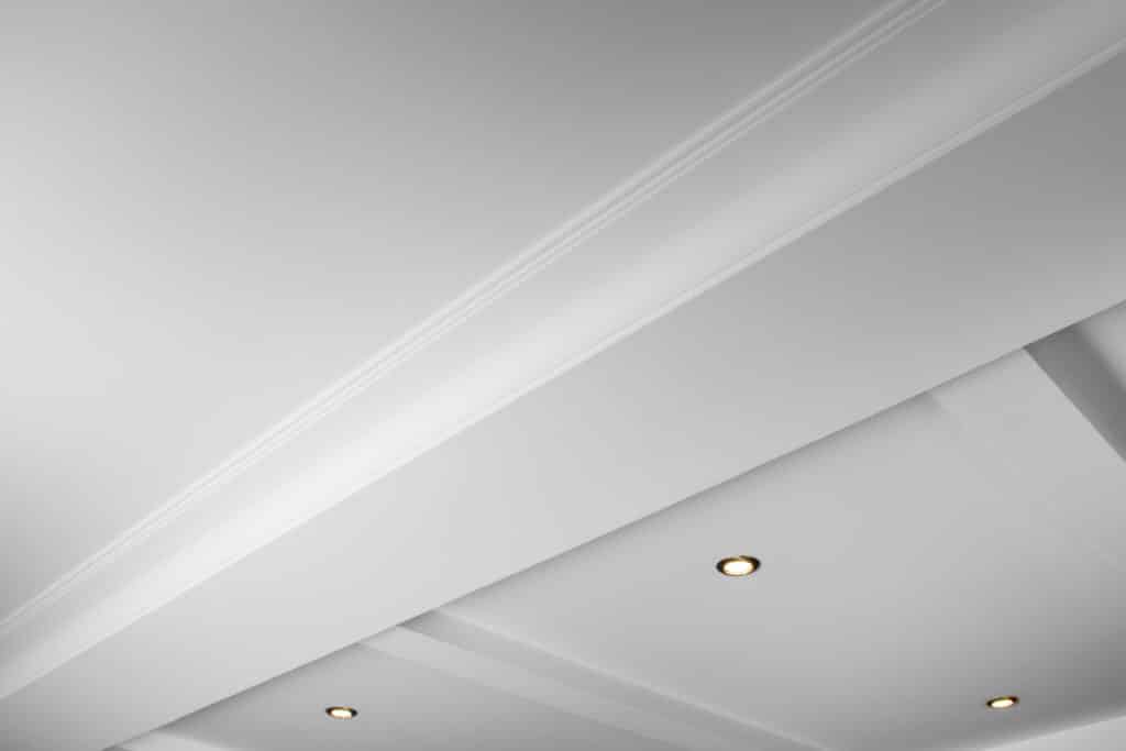 Plafond blanc moderne moulures et spots encastrés Plafond blanc moderne en angle avec moulures décoratives et spots encastrés lumineux créant un jeu d'ombres et de lumières.
