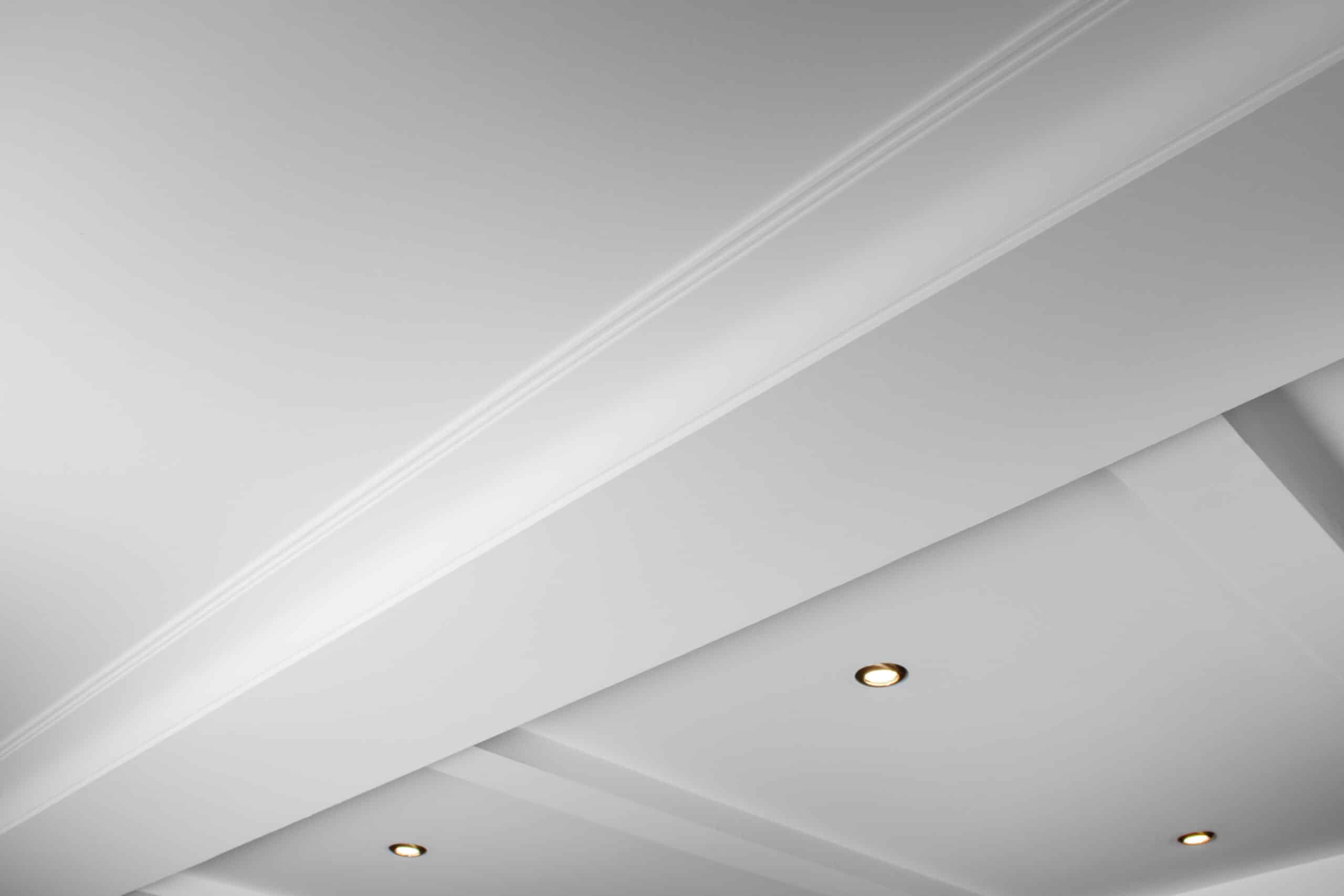 Plafond blanc moderne en angle avec moulures décoratives et spots encastrés lumineux créant un jeu d'ombres et de lumières.