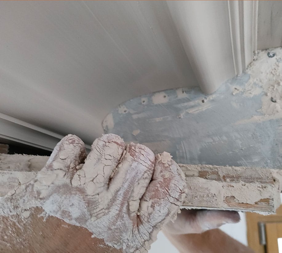 Application d'enduit : Finition joint de moulure au plafond Mains gantées et couvertes de plâtre appliquant de l'enduit pour joindre une cimaise ou moulure au plafond.