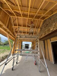 Charpentier souriant sur échafaudage posant l'isolation Pavatet sous une charpente bois en cours de rénovation.