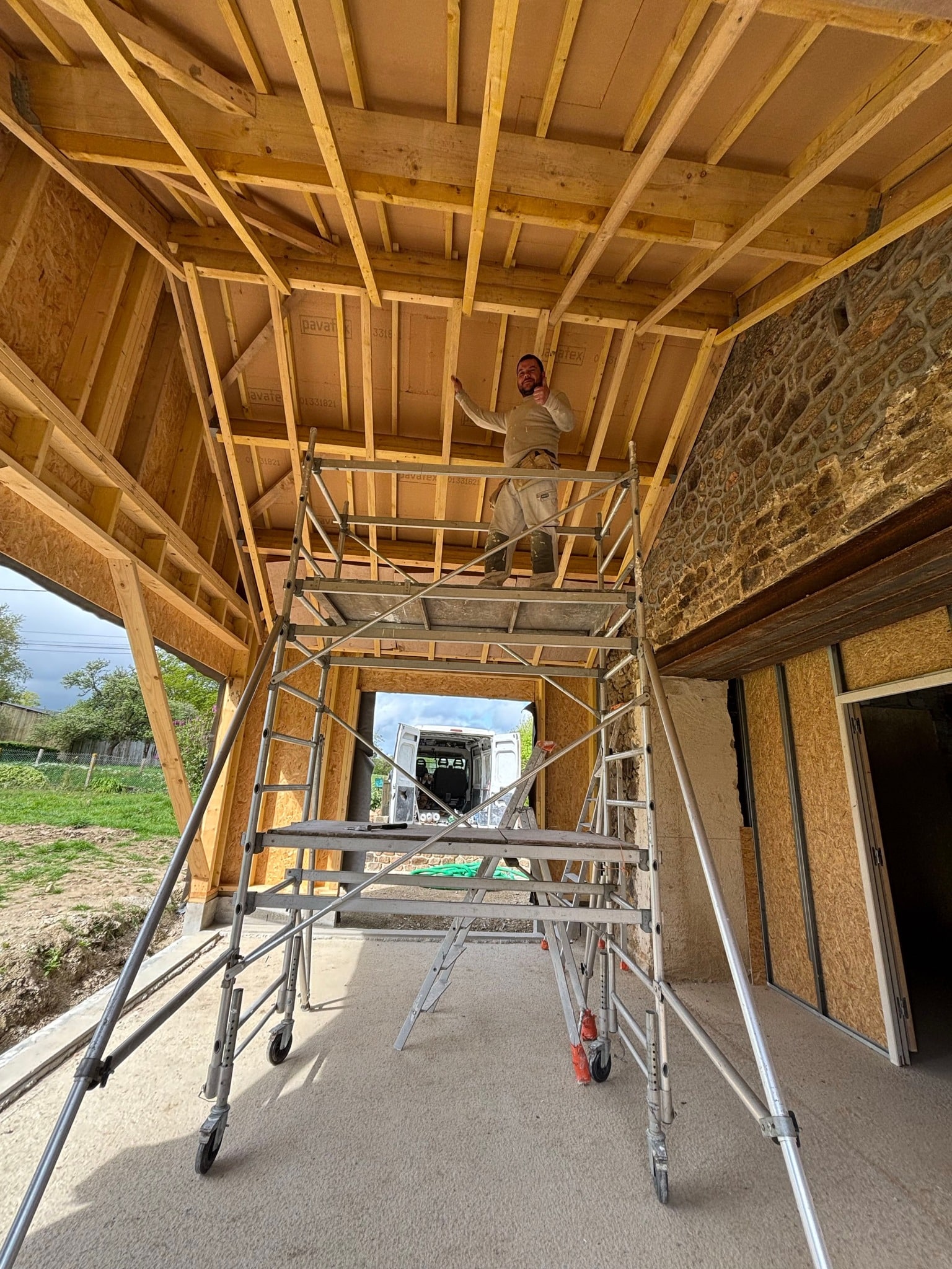 Charpentier souriant sur échafaudage posant l'isolation Pavatet sous une charpente bois en cours de rénovation.