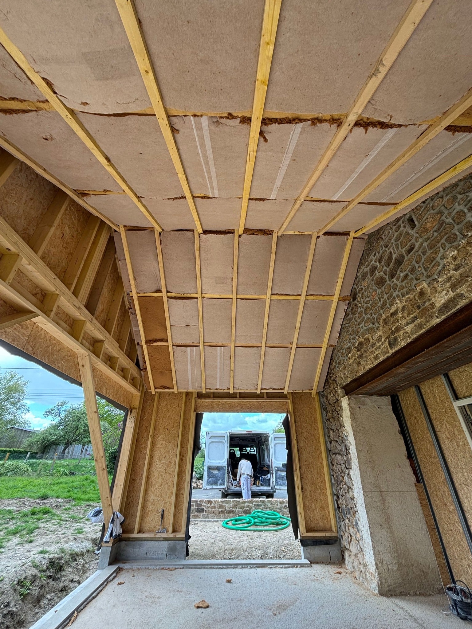 Chantier d'extension en bois avec pose d'isolation biosourcée entre chevrons, jouxtant un mur en pierre naturelle.
