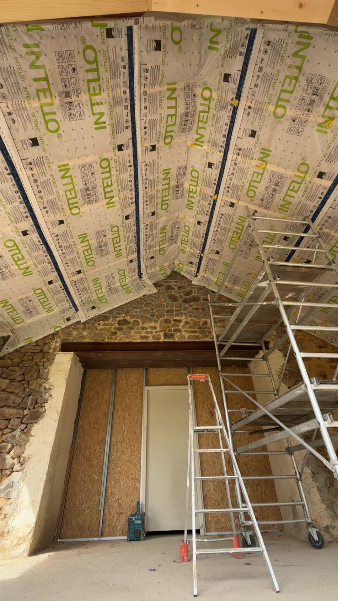Pose de membrane d'étanchéité INTELLO au plafond, murs en pierre et échafaudage sur chantier de rénovation énergétique.