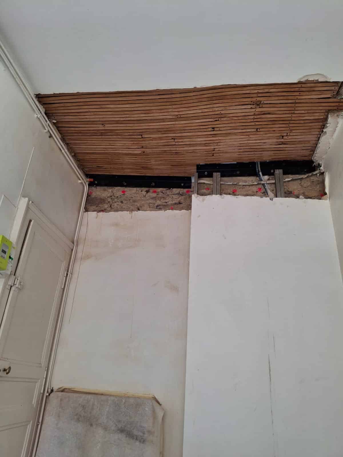 Rénovation d'un plafond à lattes en bois avec poutre métallique IPN et mur en pierre apparente.